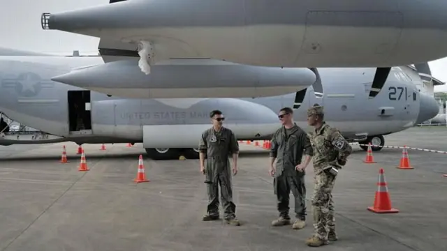 Três oficiais conversam ao lado de um avião militar americano